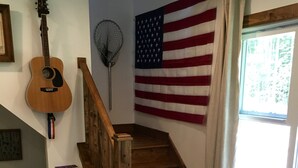 A staircase with a wooden handrail, an American flag, a guitar, and a fan on the wall. - Solar powered cottage at lake, with dock, on private 300 acre timber preserve (Clarksville)