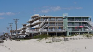 Ein mehrstöckiges Hotel direkt am Strand mit Balkonen, Sitzgelegenheiten im Freien und einem Schild mit der Aufschrift 'Four Winds'.