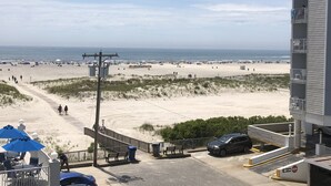 Blick auf einen Strand mit einem Parkplatz, einem Gebäude mit Balkonen und einer Promenade, die zum Strand führt.