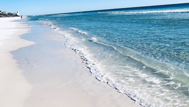 A beach with clear water, a sandy shore, and a few buildings in the background. - Private Beach Access Gulf-View Penthouse 3BR/3BA Near Seaside (Seagrove Beach)