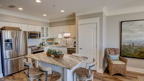 A modern kitchen with white cabinetry, stainless steel appliances, a marble countertop, and a dining area with wicker chairs. - Private Beach Access Gulf-View Penthouse 3BR/3BA Near Seaside (Seagrove Beach)