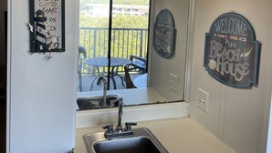 A kitchen with a sink, two pendant lights, and a view of a balcony with outdoor furniture. - HHI Beach & Tennis #AR416, 2BR2BA, top 4th fl, angled Oceanfront condo, 6 max. (Hilton Head Island)