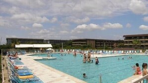 A swimming pool with multiple lanes, surrounded by lounge chairs and umbrellas, with buildings in the background. - HHI Beach & Tennis #AR416, 2BR2BA, top 4th fl, angled Oceanfront condo, 6 max. (Hilton Head Island)