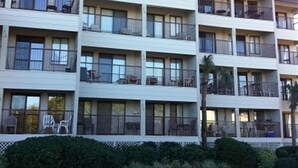 A multi-story hotel with balconies, large windows, and a parking lot in front. - HHI Beach & Tennis #AR416, 2BR2BA, top 4th fl, angled Oceanfront condo, 6 max. (Hilton Head Island)
