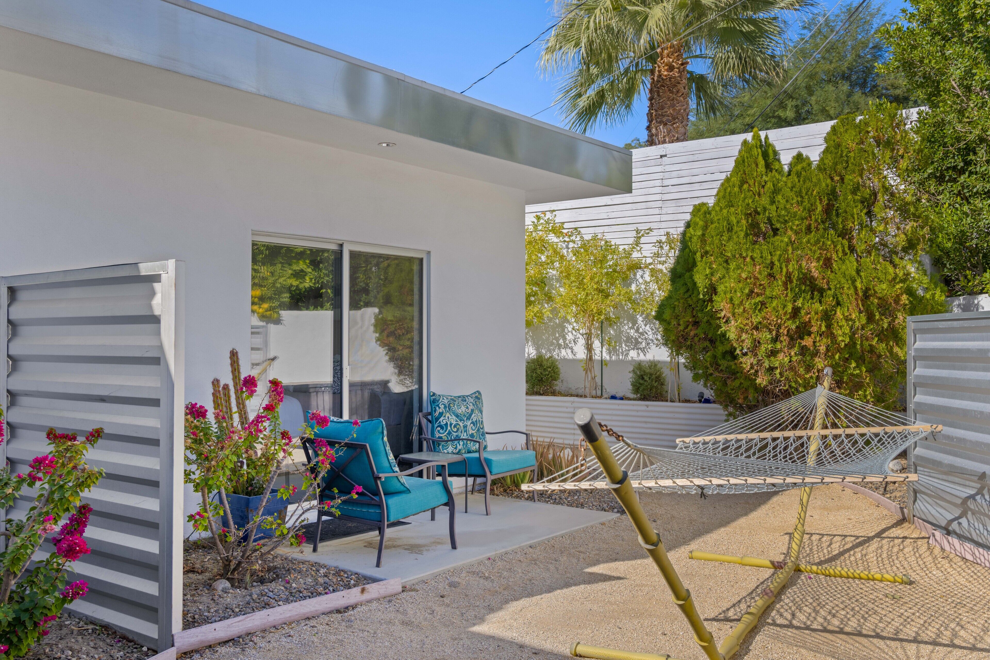 Una casa moderna amb un pati que disposa d'unes cadires, plantes en testos i una cadira espanyola.