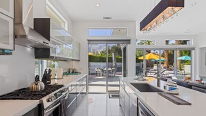 A modern kitchen with a gas stove, stainless steel appliances, and a large window overlooking a patio area. - Spring into Palm Springs and escape winter! (Palm Springs)