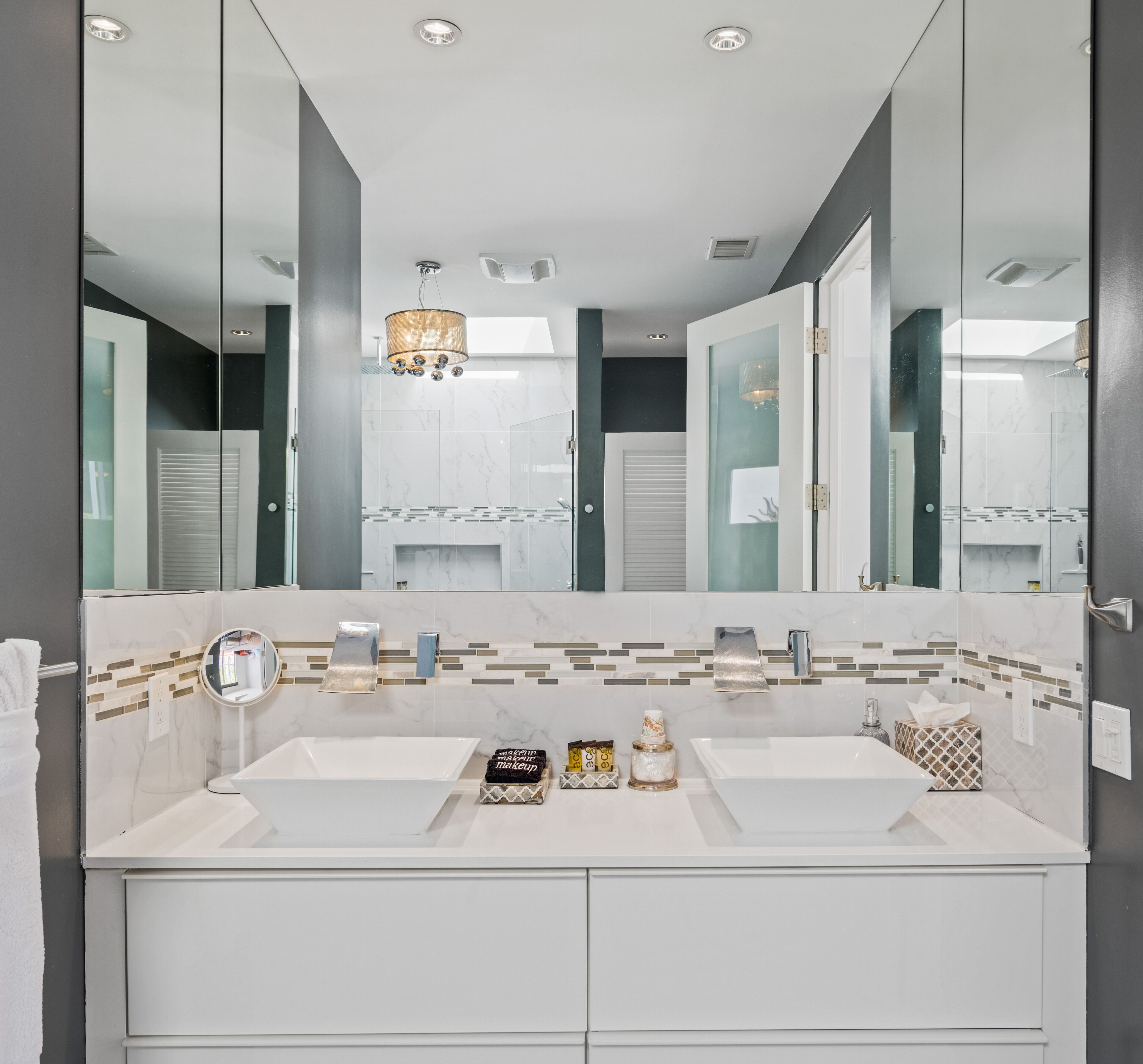 A modern bathroom with a large mirror, two sinks, and a vanity.