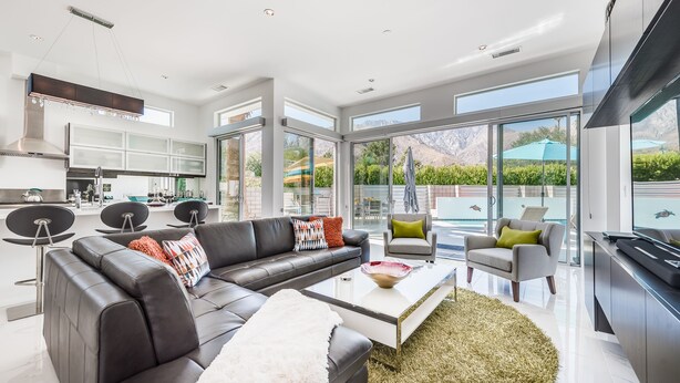 A modern living room with a black leather sofa, a glass coffee table, and a view of a pool and mountains. - Spring into Palm Springs and escape winter! (Palm Springs)