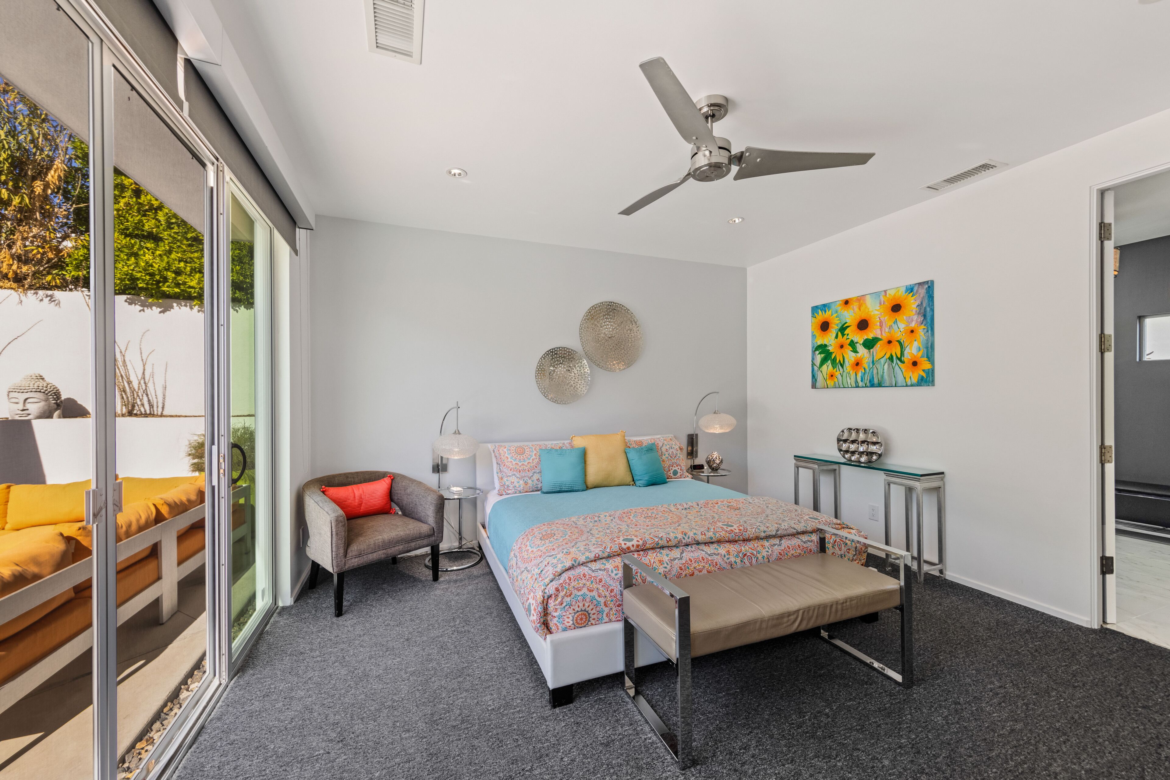 A modern bedroom with a bed, a chair, a ceiling fan, and a painting.