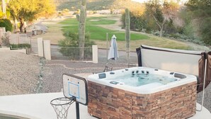 A hot tub with a stone exterior, a basketball hoop, and a view of a golf course. - 4 Bedroom Single Story Golf Course Home, Heated Diving Pool + Slide, & Hot Tub  (Phoenix)