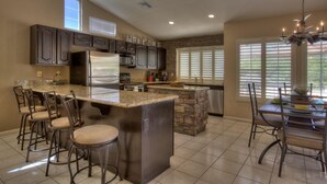 A kitchen with a central island, bar stools, a dining table with chairs, a chandelier, and a stone accent wall. - 4 Bedroom Single Story Golf Course Home, Heated Diving Pool + Slide, & Hot Tub  (Phoenix)