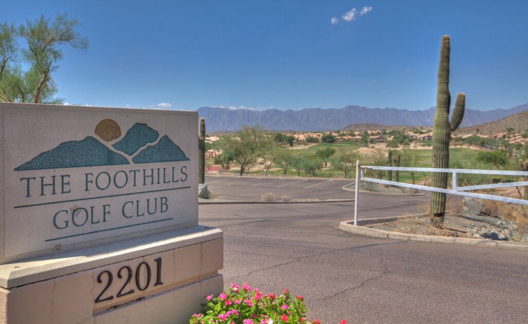 A sign for The Foothills Golf Club with a mountainous landscape in the background.