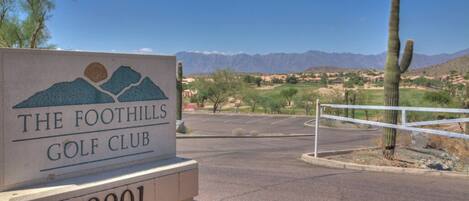 A sign for The Foothills Golf Club with a mountainous landscape in the background.