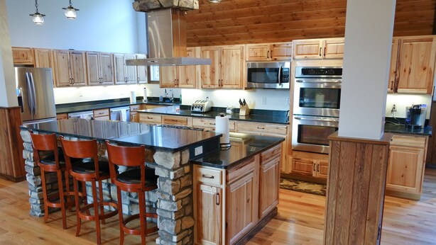 A spacious kitchen with wooden cabinets, a central island with stools, and modern appliances including a refrigerator, microwave, and oven. - Westcott House- Privacy, amenities and space all in one beautiful package! (Luray)