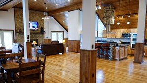 A spacious living area with a wooden floor, a stone fireplace, a television, and a kitchen with wooden cabinets and a stone accent wall. - Westcott House- Privacy, amenities and space all in one beautiful package! (Luray)