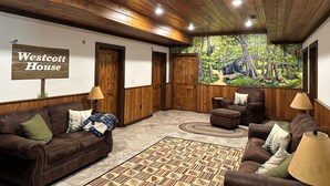 A cozy room with wooden walls and ceiling, a large forest mural, a sign reading 'Westcott House', and leather sofas with lamps. - Westcott House- Privacy, amenities and space all in one beautiful package! (Luray)