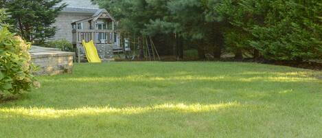A backyard with a wooden deck, a slide, and a large tree.