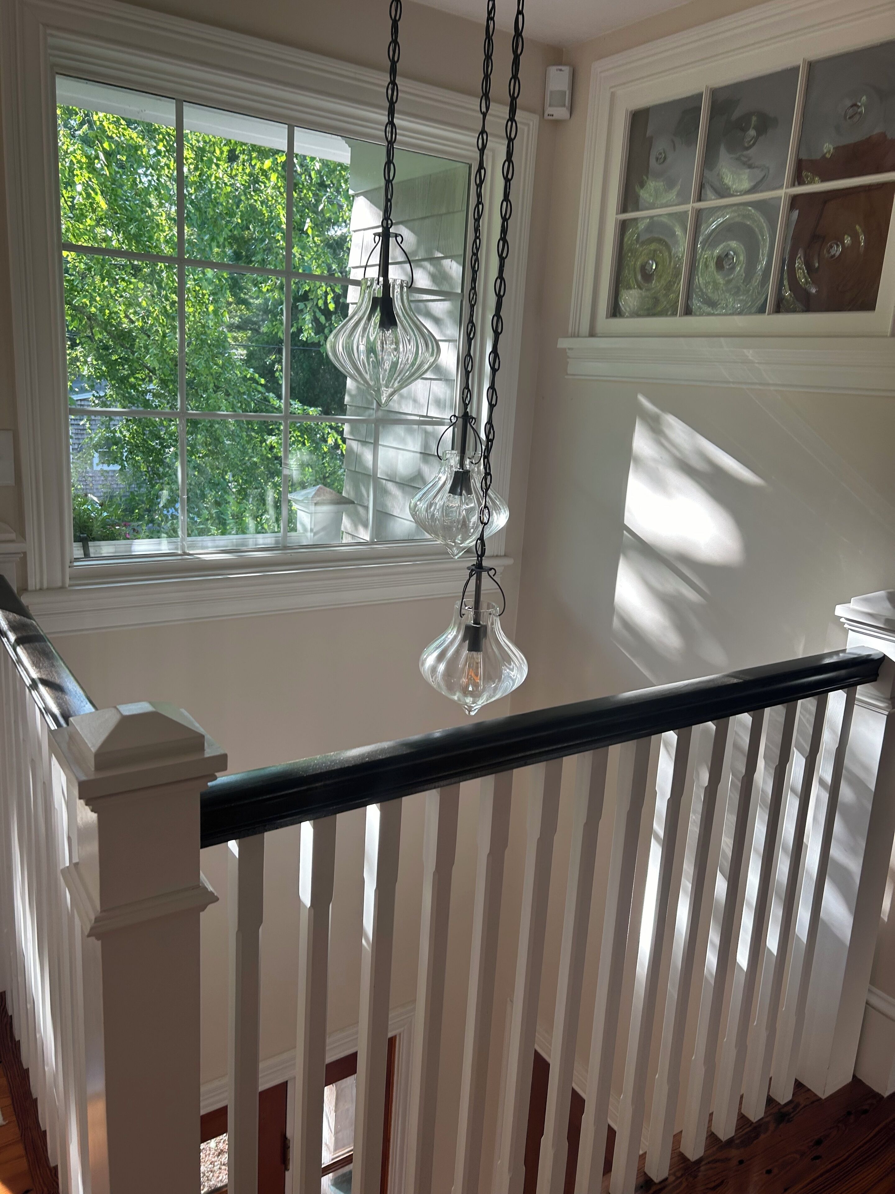 Ein Zimmer mit weißer Geländer, einem Fenster mit Jalousien und einer Pendelleuchte.