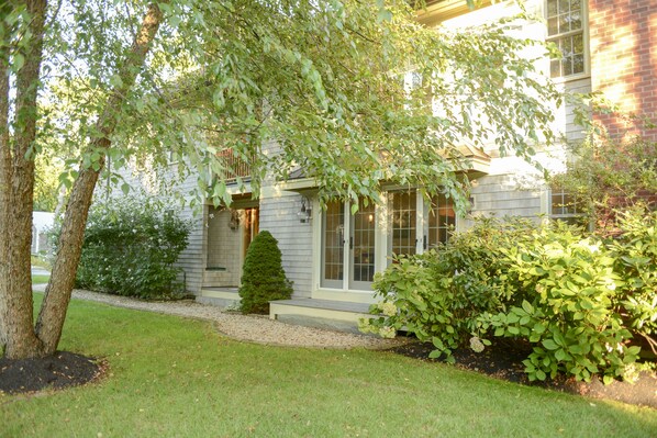 Une maison à deux étages avec un porche à l’avant, un petit arbre et une pelouse bien entretenue.