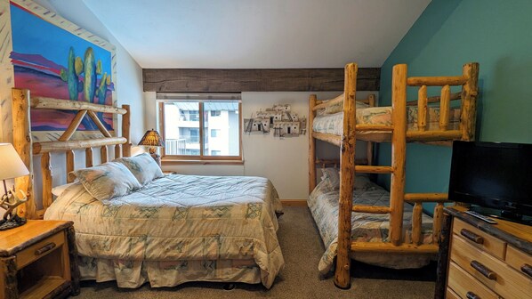 A rustic room with a bunk bed, a single bed, a TV, and a mural on the wall.