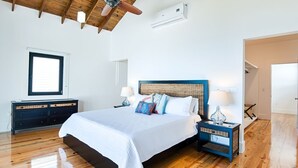 Ein Schlafzimmer mit Holzboden, einem Bett mit weißer Bettwäsche, zwei Nachttischen mit Lampen und einem Fenster mit Jalousien.
