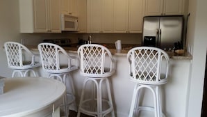 A kitchen with white cabinets, a microwave, a refrigerator, and three white bar stools. - Beautiful Furnished In the Courtyard, Right Beside The Pool On 1st Floor (Gulf Shores)