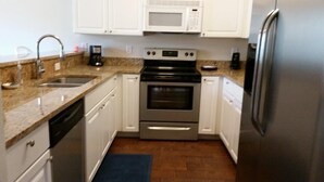 A compact kitchen with white cabinets, a stainless steel refrigerator, a microwave, a stove, and a dishwasher. - Beautiful Furnished In the Courtyard, Right Beside The Pool On 1st Floor (Gulf Shores)