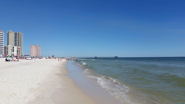 A beach with a pier extending into the ocean, surrounded by high-rise buildings. - Beautiful Furnished In the Courtyard, Right Beside The Pool On 1st Floor (Gulf Shores)