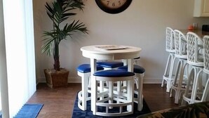 A dining area with a round table and chairs, a potted plant, and a wall clock. - Beautiful Furnished In the Courtyard, Right Beside The Pool On 1st Floor (Gulf Shores)