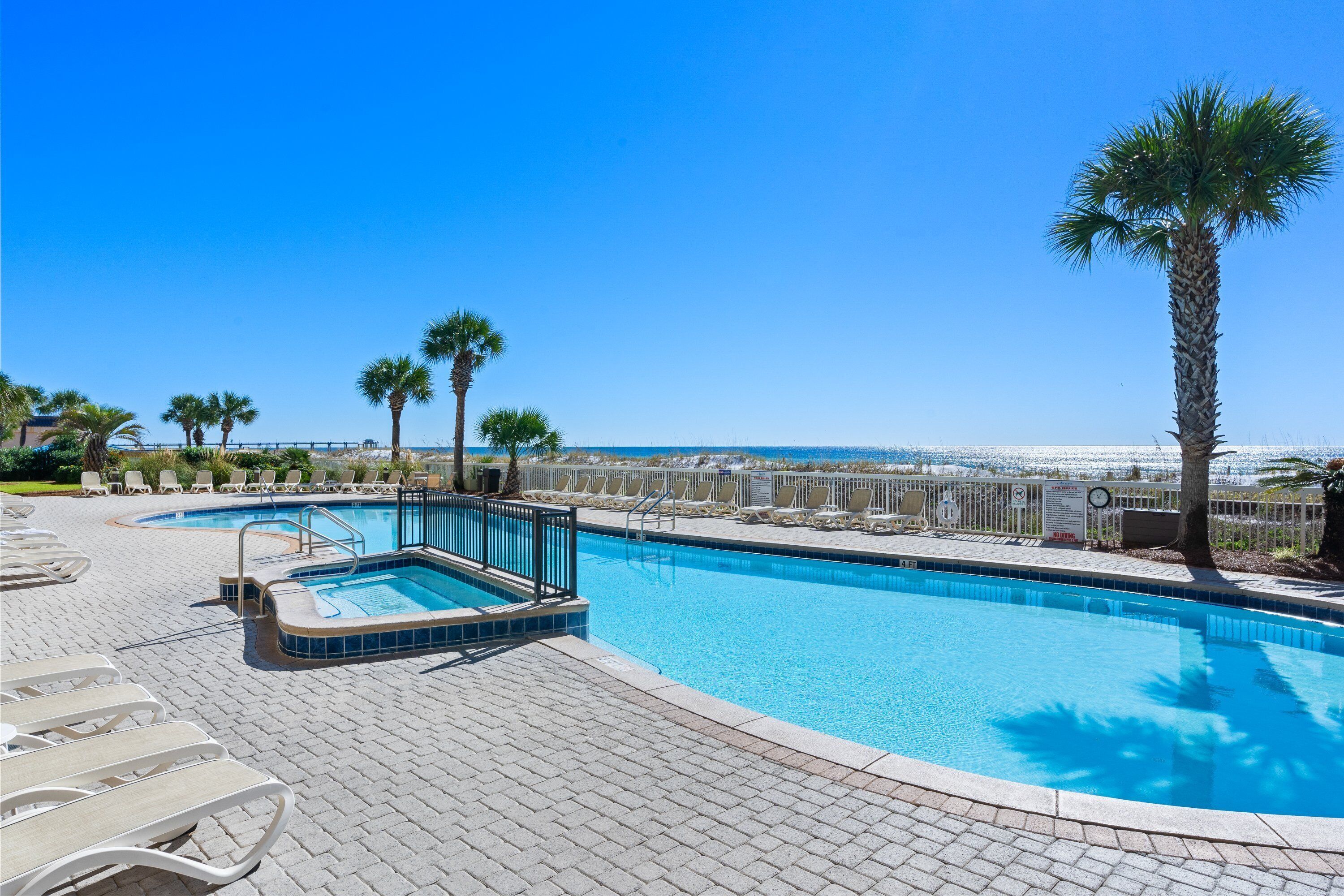A swimming pool with lounge chairs and palm trees, overlooking a beach.