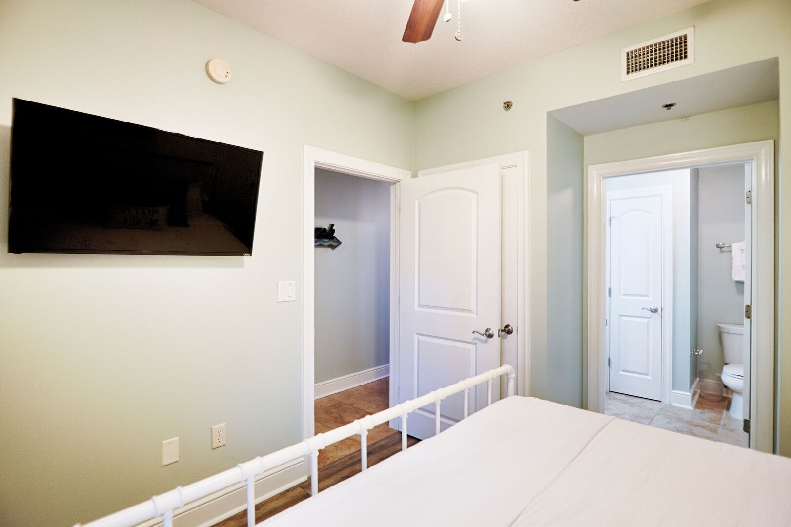 A bedroom with a bed, a TV mounted on the wall, and a bathroom visible through an open door.