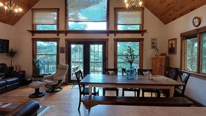 A spacious living room with a wooden dining table, comfortable seating, large windows, and a television. - Minutes from Deep Creek Lake, Located on 24-acre farm with private 1-acre lake (Accident)