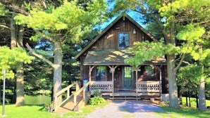 A rustic wooden cabin with a porch, surrounded by trees and a gravel path. - Minutes from Deep Creek Lake, Located on 24-acre farm with private 1-acre lake (Accident)