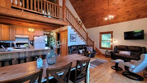A spacious living area with a wooden staircase, a dining table with chairs, a leather sofa, and a television mounted on the wall. - Minutes from Deep Creek Lake, Located on 24-acre farm with private 1-acre lake (Accident)