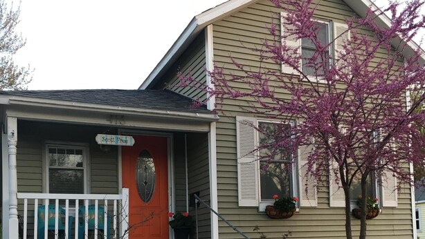 A house with a porch, a red door, and a small tree with pink flowers.