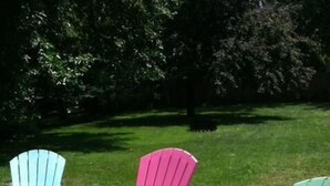 Three Adirondack chairs in different colors (light blue, pink, and green) arranged on a grassy lawn.