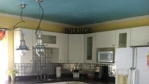 A kitchen with white cabinets, a central island, a microwave, a refrigerator, and hanging pendant lights.