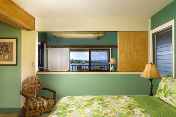 A bedroom with a view of the ocean, a bed with a floral bedspread, a wooden chair, and a window with a view of the sea. - Oceanview #201 at Hana Kai Maui - 1 Bedroom Upper Floor Corner, Panoramic View! (Hana)