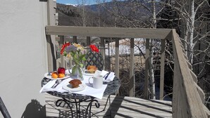 A balcony with a table set for a meal, featuring a plate of food, a vase with flowers, and a cup. - Sonnenblick 6: Ski In, Pool, Hot Tub, In the Heart of Snowmass, No Car Needed  (Snowmass Village)
