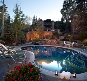 A serene indoor pool area with lounge chairs, a stone wall, and a view of a multi-story building. - Sonnenblick 6: Ski In, Pool, Hot Tub, In the Heart of Snowmass, No Car Needed  (Snowmass Village)