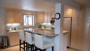 A kitchen with a central island, bar stools, a clock, and modern appliances. - Sonnenblick 6: Ski In, Pool, Hot Tub, In the Heart of Snowmass, No Car Needed  (Snowmass Village)
