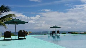 Ein Poolbereich mit Liegestühlen und Sonnenschirmen, mit Blick auf den Ozean und einem gefliesten Deck.