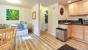 A cozy living room with a sofa, wooden dining table, and a kitchen area with wooden cabinets and a microwave. - The Cascade River Trail Retreat - a short walk to river & downtown! Pets OK! (Bend)