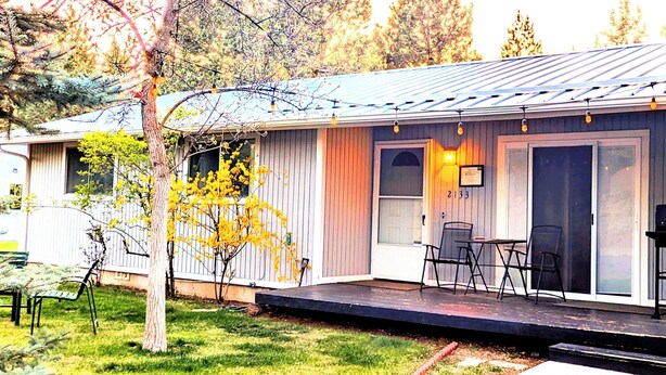 A single-story mobile home with a porch, outdoor seating, and a small yard. - The Cascade River Trail Retreat - a short walk to river & downtown! Pets OK! (Bend)