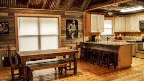 Una cocina rústica con pisos de madera, una gran mesa de comedor con bancos y una zona de bar.
