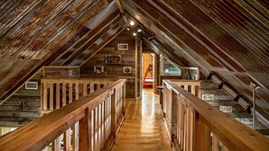 Un ático con vigas de madera, una escalera de madera y una puerta visible que da a otra habitación.