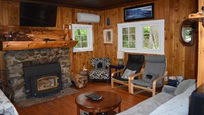 A log cabin interior with a stone fireplace, wooden walls, a television, and a cozy seating area. - The Cornerstone Cabin - Mount Rainier (Ashford)