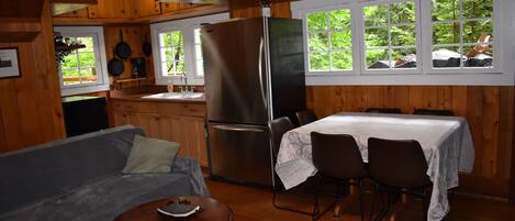 A cabin interior with a sofa, dining table, chairs, a refrigerator, and a kitchen area with a sink and window.