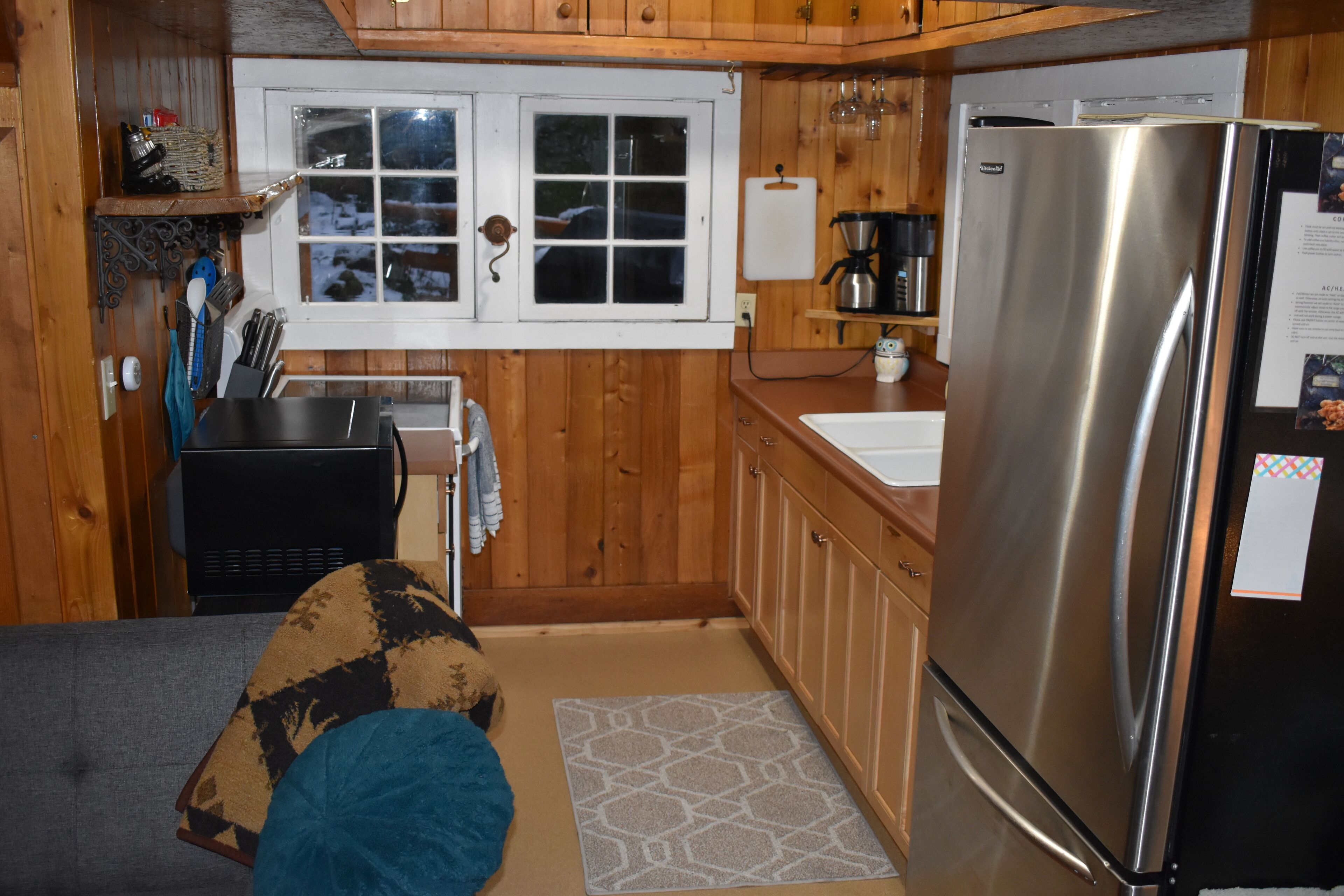 Una cocina compacta con armarios de madera, un refrigerador de acero inoxidable, una ventana con vistas y un lavamanos pequeño.