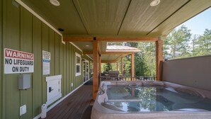 Un bain à remous sur une terrasse en bois, avec un espace couvert, un panneau d’avertissement concernant la présence d’un sauveteur et un panneau indiquant les règles du spa.